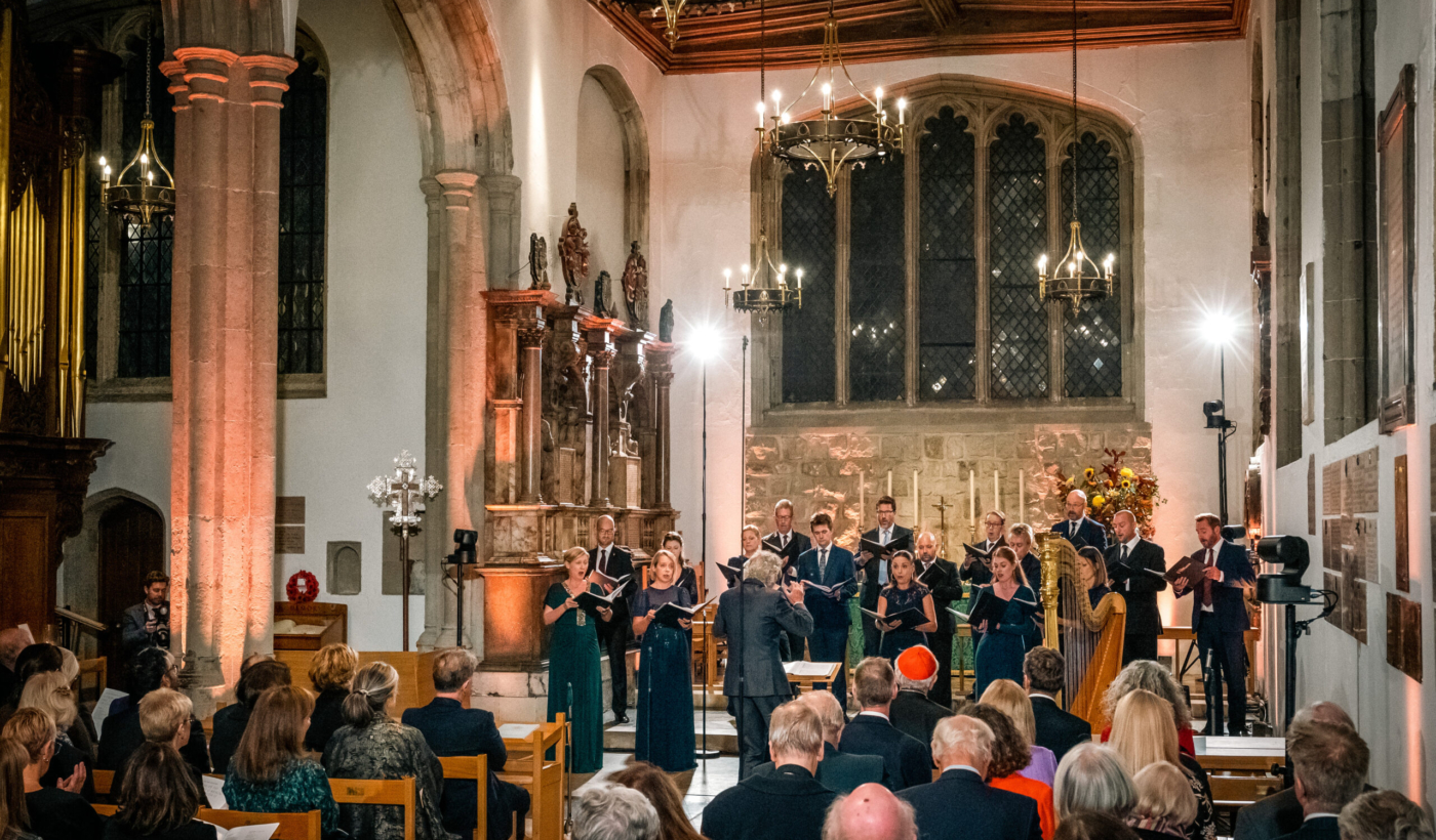 Harry Christophers conducting The Sixteen inside the Chapel Royal of St Peter ad Vincula. A seated audience watch them perform.