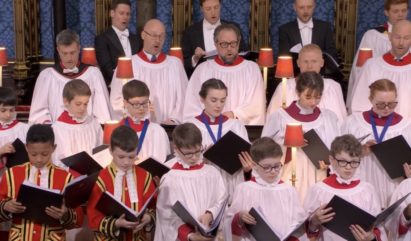 Rows of singers holding scores and singing out. In the top right is Genesis Sixteen alumni Alexander Hume.