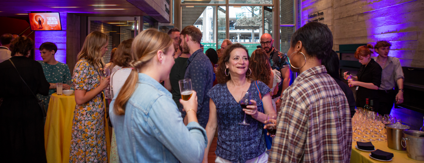 Inside a large foyer with stone walls, groups of people stood holding glasses of wine and chatting with each other.